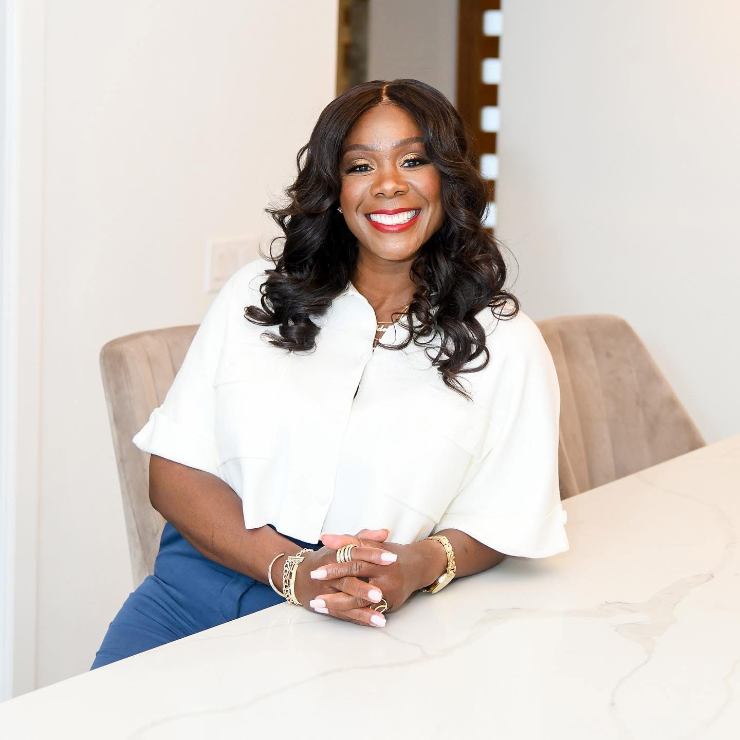 Dana Reshay seated at a counter, smiling with hands folded